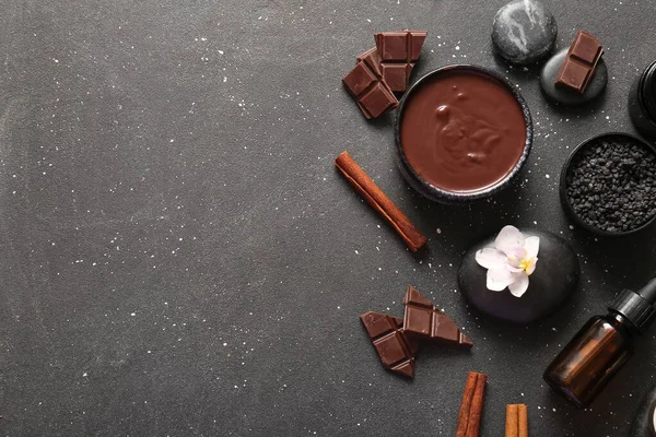 Bir kase erimiş çikolatalı spa kompozisyonu, çikolata parçaları ve siyah arka planda spa taşları