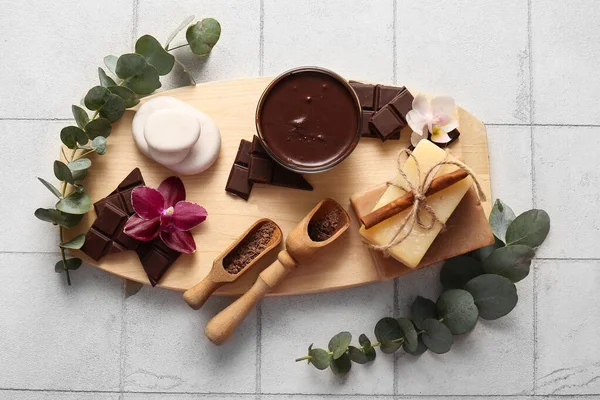 Ahşap tepsiyle spa kompozisyonu, bir kase erimiş çikolata, kaplıca taşları ve fayans zemininde sabun.