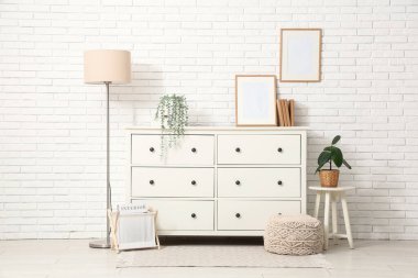 Beyaz tuğla duvarın yanındaki çekmeceleri ve lambasıyla modern oturma odasının şık bir iç mekanı.