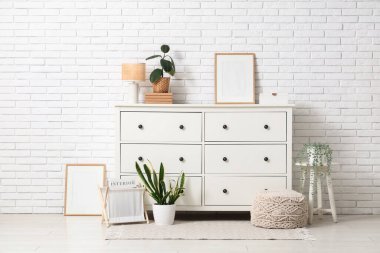 Oturma odasının iç tarafındaki beyaz tuğla duvarın yanındaki çekmeceler, lambalar ve bitkiler.