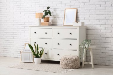 Oturma odasının iç tarafındaki beyaz tuğla duvarın yanındaki çekmeceler, lambalar ve bitkiler.