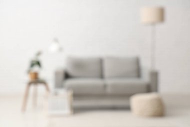 Oturma odasının bulanık manzarası, yerde lamba ve beyaz tuğla duvarın yanındaki kanepe.