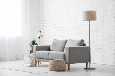 Beyaz tuğla duvarın yanında kanepesi ve lambası olan oturma odasının içinde.