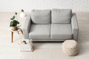 Oturma odasının içinde kanepe, lamba ve beyaz tuğla duvarın yanındaki masa.