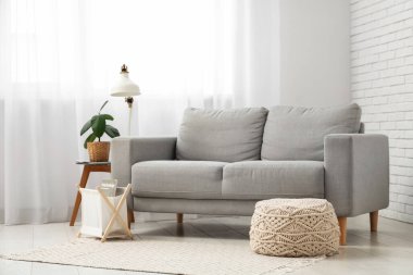 Beyaz tuğla duvarın yanındaki masa üzerinde kanepe ve lambayla oturma odasının içinde.