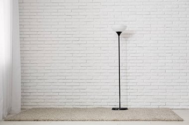 Beyaz tuğla duvarın yanında yer lambası var.