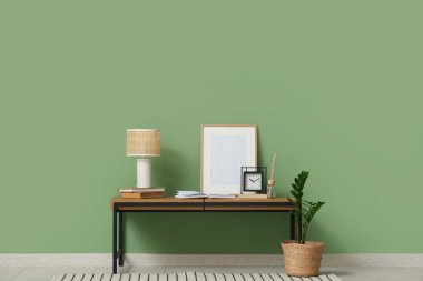 Oturma odasının içinde yeşil duvarın yanında bank, lamba ve fotoğraf çerçevesi var.