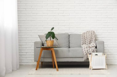 Beyaz tuğla duvarın yanında kanepesi ve masası olan modern oturma odasının içinde.