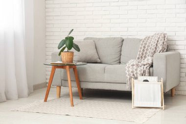 Beyaz tuğla duvarın yanında kanepesi ve masası olan modern oturma odasının içinde.