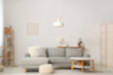 Oturma odasının bulanık manzarası, kanepe, puf ve beyaz duvarın yanındaki masa.