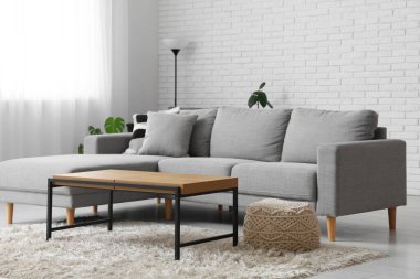 Koltuk ve masa beyaz tuğla duvarın yanında, oturma odasının içinde.