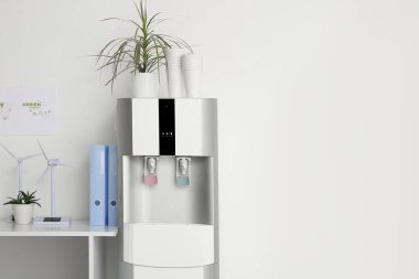 Ofiste beyaz duvarın yanında kağıt bardakları ve işyeri olan modern su soğutucusu, yakın plan.