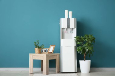 Modern su soğutucusu, masa ve tesis mavi duvarın yanında.