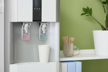 Oda yeşil duvarın yanında kağıt bardak ve raf üniteli modern su soğutucusu.