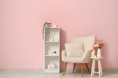 Modern oturma odasının şık koltuğu ve pembe duvarın yanındaki masada yanan mumlar.