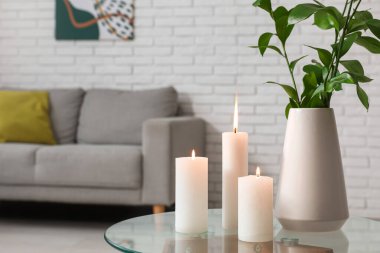 Oturma odasının iç tarafındaki masada, vazoda yanan mumlar ve yeşil dallar.