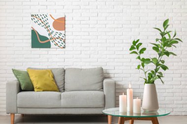 Oturma odasının masasındaki vazoda yanan mumlar ve yeşil dallar.