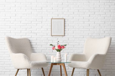 Oturma odasının içinde koltuklar ve yanan mumlar beyaz tuğla duvarın yanında.