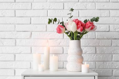 Beyaz tuğla duvarın yanındaki çekmecelerde lale çiçekleri olan mumlar ve vazolar yakılıyor.