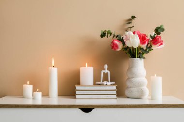 Odadaki bej duvarın yanındaki çekmecelerde mumlar, kitaplar ve çiçekler yakılıyor.