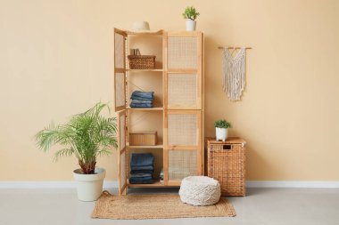 Odanın içindeki bej duvarın yanında giysi ve sepetli ahşap dolabı aç.