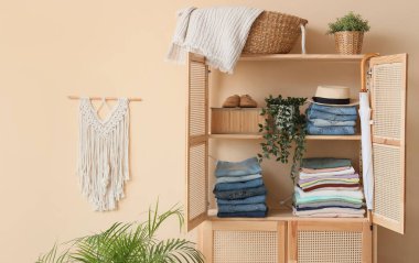 Odanın iç tarafındaki bej duvarın yanında giysileri ve çiçekleri olan ahşap dolap, yakın plan.