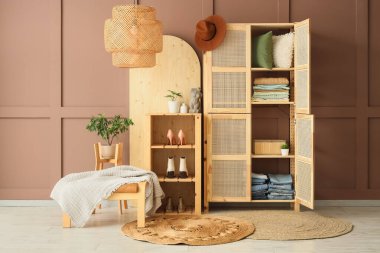 Odanın içindeki kahverengi duvarın yanında giysiler ve yastıklar olan ahşap dolabı aç.