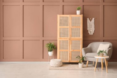 Ahşap dolap, rahat koltuk ve odanın içindeki kahverengi duvarın yanındaki puf.