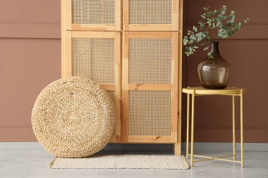 Ahşap dolap, masa ve vazo, odanın içinde kahverengi duvarın yanında yeşil dallar var.