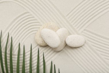 Spa taşları, tropikal yaprak ve arka plan olarak kumdaki çizgiler, yakın plan. Zen kavramı