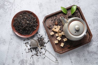 Siyah çay yapraklı tabak ve gri arka planda çaydanlık.