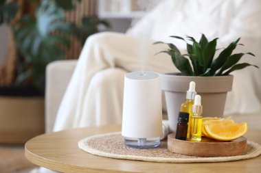 Evde oturan kadına karşı yağlı, turuncu ve bitkili hava nemlendirici, yakın plan.