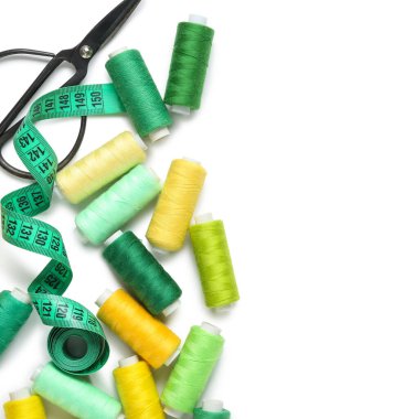 Beyaz zemin üzerinde makas ve mezura ile birçok iplik makarası