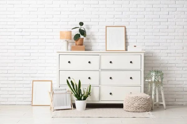 Oturma odasının iç tarafındaki beyaz tuğla duvarın yanındaki çekmeceler, lambalar ve bitkiler.