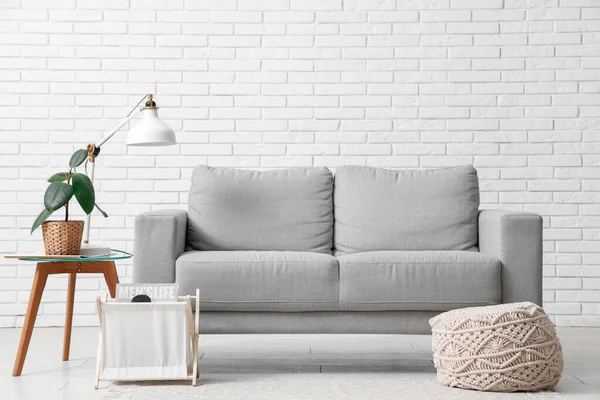 Oturma odasının içinde kanepe, lamba ve beyaz tuğla duvarın yanındaki masa.