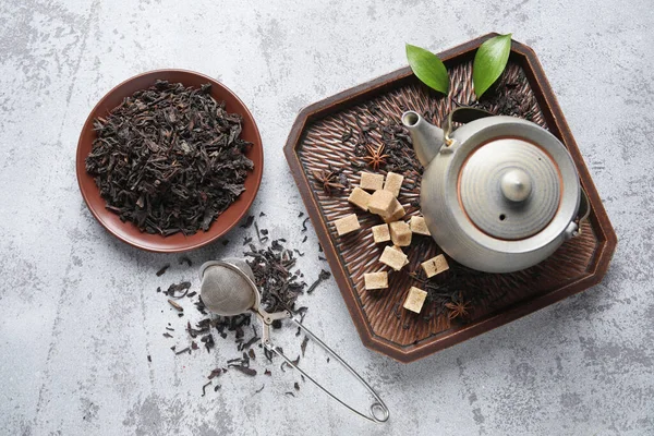 Siyah çay yapraklı tabak ve gri arka planda çaydanlık.