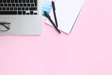 Pembe arka planda modern dizüstü bilgisayarı, defteri ve kalemleri olan grafik tasarımcılarının çalışma yeri