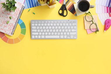 Klavye, renk grafikleri ve sarı arka planda bir fincan kahveyle grafik tasarımcının çalışma yeri