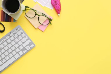 Sarı arka planda klavye, gözlük ve kahve ile grafik tasarımcısının çalışma yeri