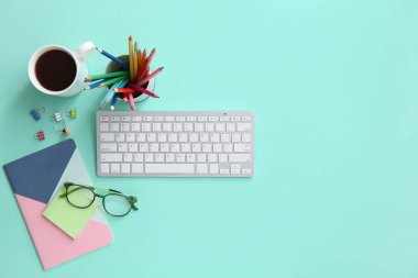 Grafik tasarımcısının klavyesi, kahve fincanı ve turkuaz arka plan kırtasiyesi olan çalışma yeri