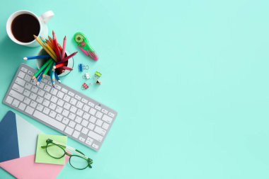 Grafik tasarımcısının klavyesi, kahve fincanı ve turkuaz arka plan kırtasiyesi olan çalışma yeri