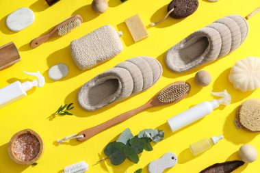 Ayak masajı için farklı banyo malzemeleri ve sarı arka planda terlikler.