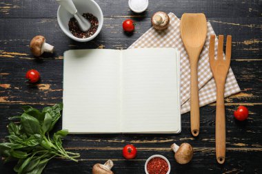 Siyah ahşap zemin üzerinde boş tarif defteri, baharatlar ve peçeteyle kompozisyon