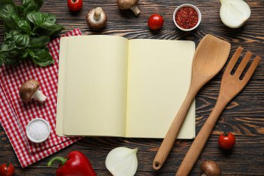Siyah ahşap zemin üzerine boş tarif defteri, çatal bıçak takımı ve malzeme içeren kompozisyon