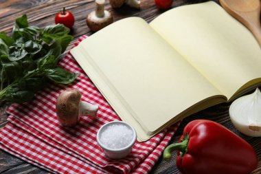 Siyah ahşap zemin üzerine boş tarif defteri, peçete ve malzeme içeren kompozisyon