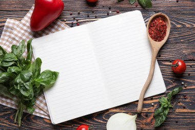 Siyah ahşap zemin üzerine boş tarif defteri, peçete ve malzeme içeren kompozisyon