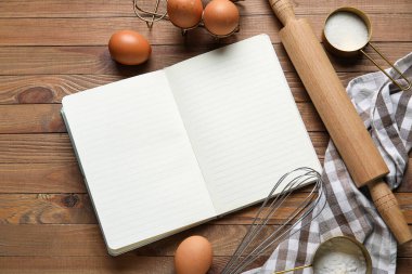 Ahşap zemin üzerinde boş tarif defteri, peçete, yumurta ve kap kacak içeren kompozisyon