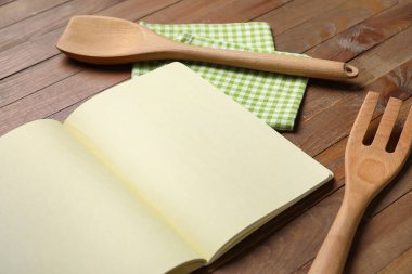 Ahşap zemin üzerinde boş tarif defteri, peçete ve ahşap çatal bıçak takımı olan kompozisyon