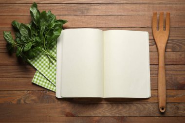 Ahşap arka planda boş tarif defteri, peçete ve yeşil yapraklar