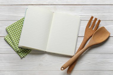 Boş tarif defteri, ahşap çatal bıçak takımı ve hafif ahşap arka planda peçete.